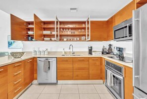 Eine moderne Küche mit Holzschränken, einem Edelstahlkühlschrank, einem Einbauofen und einer Kaffeestation.