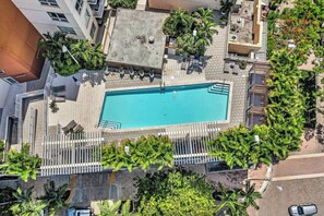 Eine Vogelperspektive zeigt ein Hotel mit einem Swimmingpool, umgeben von Palmen und einer eingezäunten Terrassenfläche.