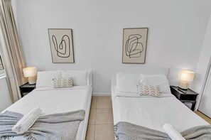 Ein Hotelzimmer mit zwei Betten, jeweils mit Kopfkissen und Decke. Es gibt zwei Nachttische mit Lampen.