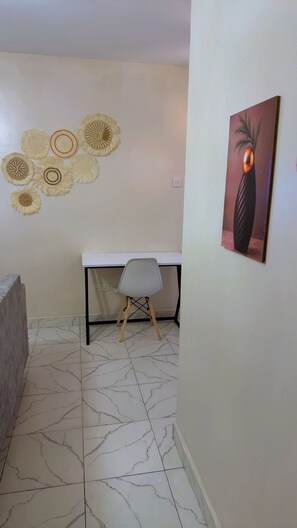 A room with a white desk, a chair, a wall with decorative wall hangings, and a tiled floor. - Thika road 1 bedroom executive  Airbnb unit located off Thika road at exit 12 (Ruiru)