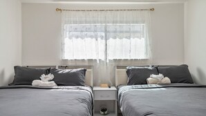 Une chambre d’hôtel avec deux lits, une table de chevet, une petite table de nuit, une horloge et une fenêtre avec des rideaux légers.