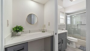Une salle de bain moderne avec un comptoir en marbre, un miroir rond, une plante en pot et une cabine de douche en verre.