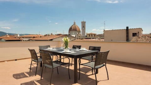 Een terras op het dak met een tafel voor vier personen, met uitzicht op een stadsgezicht met een opvallende koepel en toren.