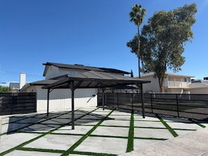 A covered patio area with a concrete floor and grass edging. - Terrific 6-bedroom house with AC in vibrant Las Vegas 10 minutes from the Strip. (Las Vegas)