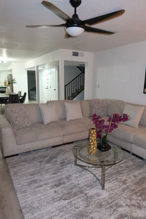 A living room with a beige sectional sofa, a glass coffee table, and a ceiling fan. - Terrific 6-bedroom house with AC in vibrant Las Vegas 10 minutes from the Strip. (Las Vegas)