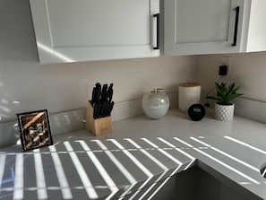 Une cuisine avec des meubles blancs, un range-couteaux, un vase décoratif, une horloge et une plante en pot.
