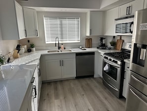 A modern kitchen with white cabinets, a stainless steel refrigerator, a built-in oven, and a coffee maker. - Terrific 6-bedroom house with AC in vibrant Las Vegas 10 minutes from the Strip. (Las Vegas)