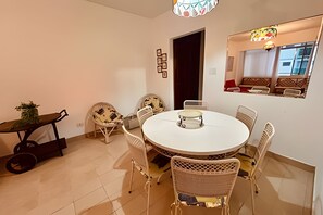A dining area with a round table, white chairs, and a small side table with a plant.