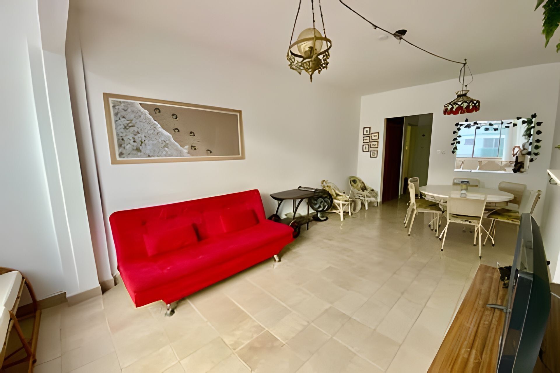 Una sala de estar con un sofá rojo, una mesa de comedor con sillas y una zona de cocina con ventana.
