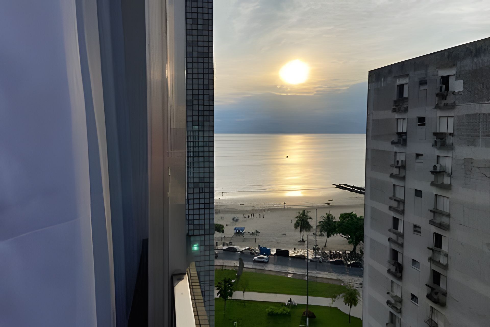 A view of a beach with a sunset, buildings in the foreground, and a clear sky.