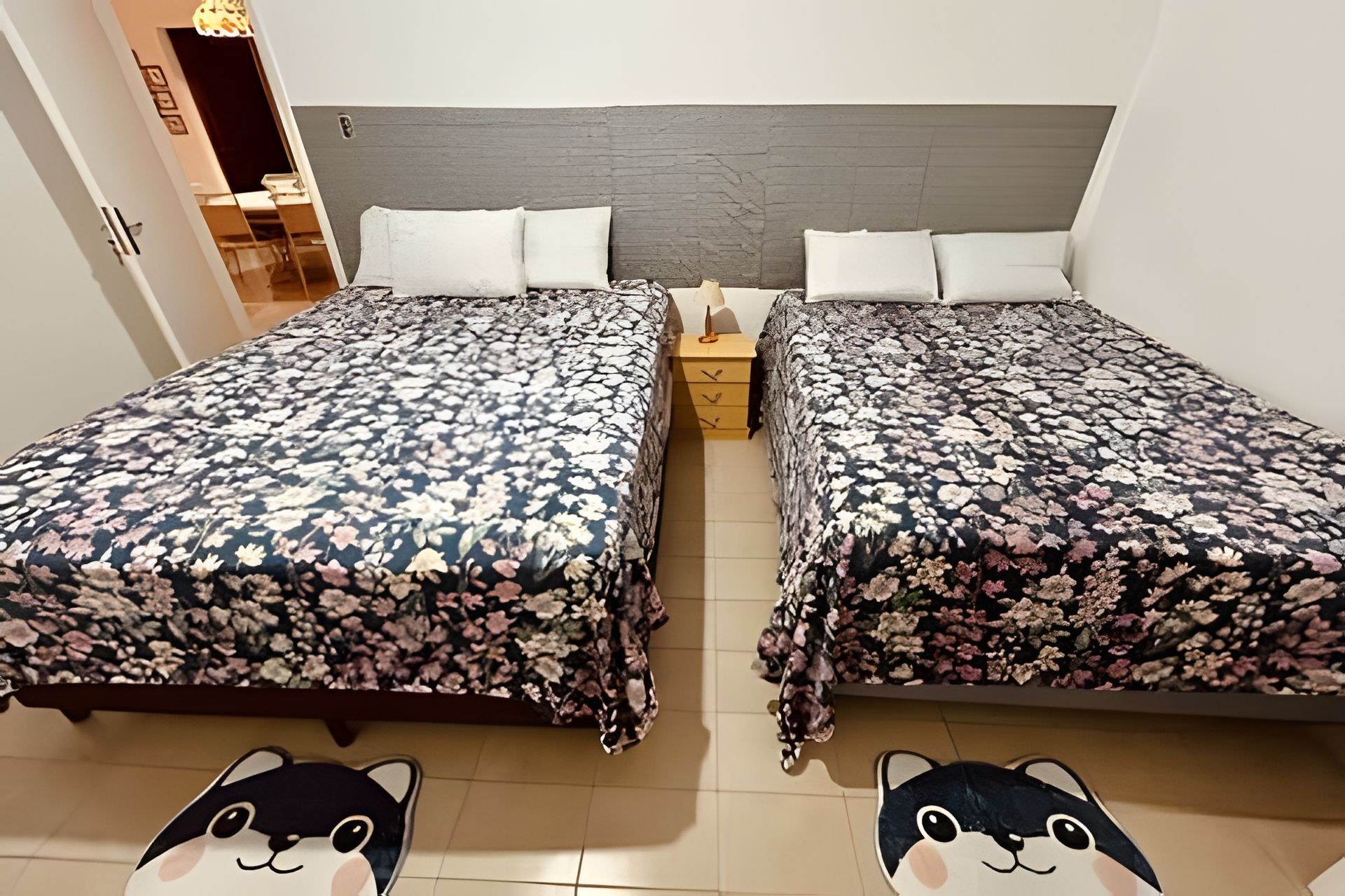 Habitación doble con dos camas, cada una con ropa de cama floral y almohadas blancas. Hay una mesita de noche de madera entre las camas.
