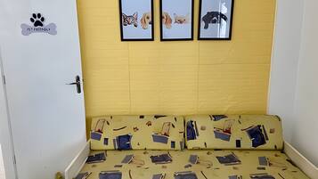 Una habitación con una pared amarilla, una puerta blanca y un sofá con funda estampada. Encima del sofá, hay tres cuadros enmarcados en la pared.