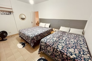 Un dormitorio con dos camas, un espejo redondo, un ventilador y una puerta que da a otra habitación.
