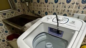 A front-loading washing machine with a control panel, a white sink, and patterned tiles on the wall.