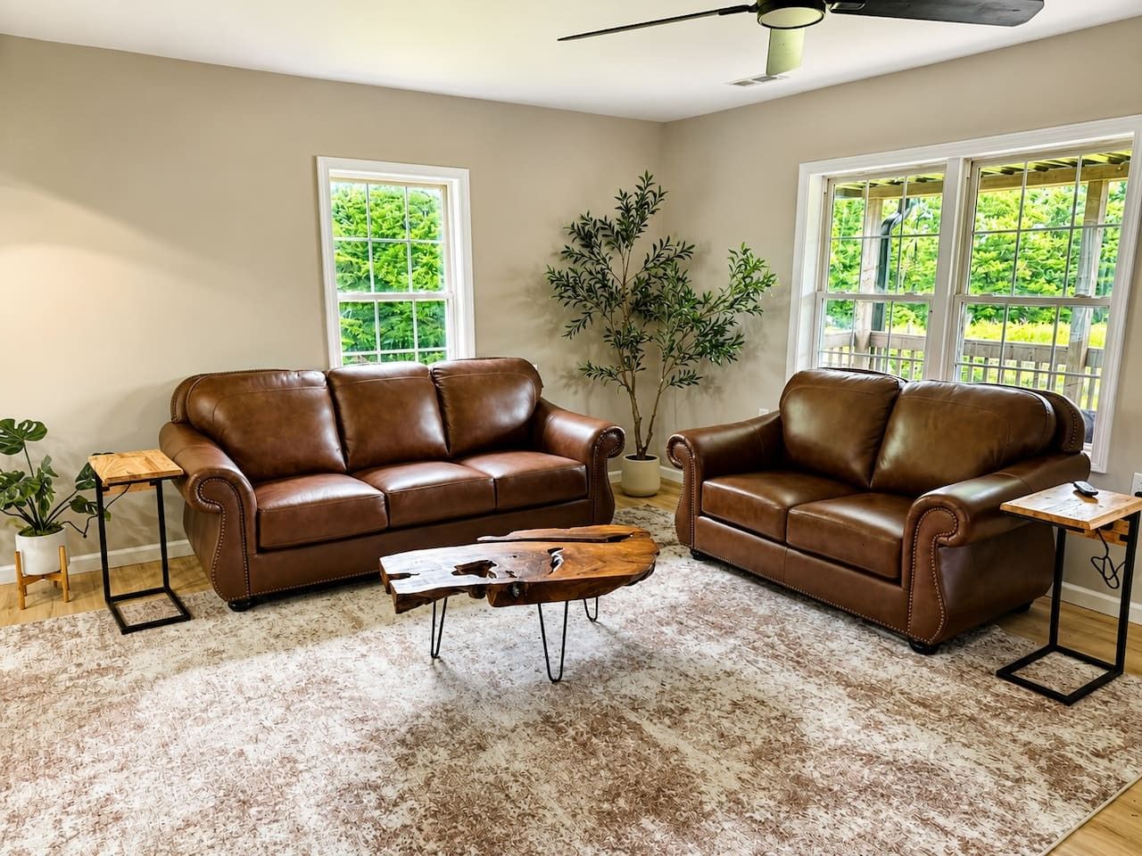 A living room with two brown leather sofas, a wooden coffee table, and a large window providing a view of greenery.
