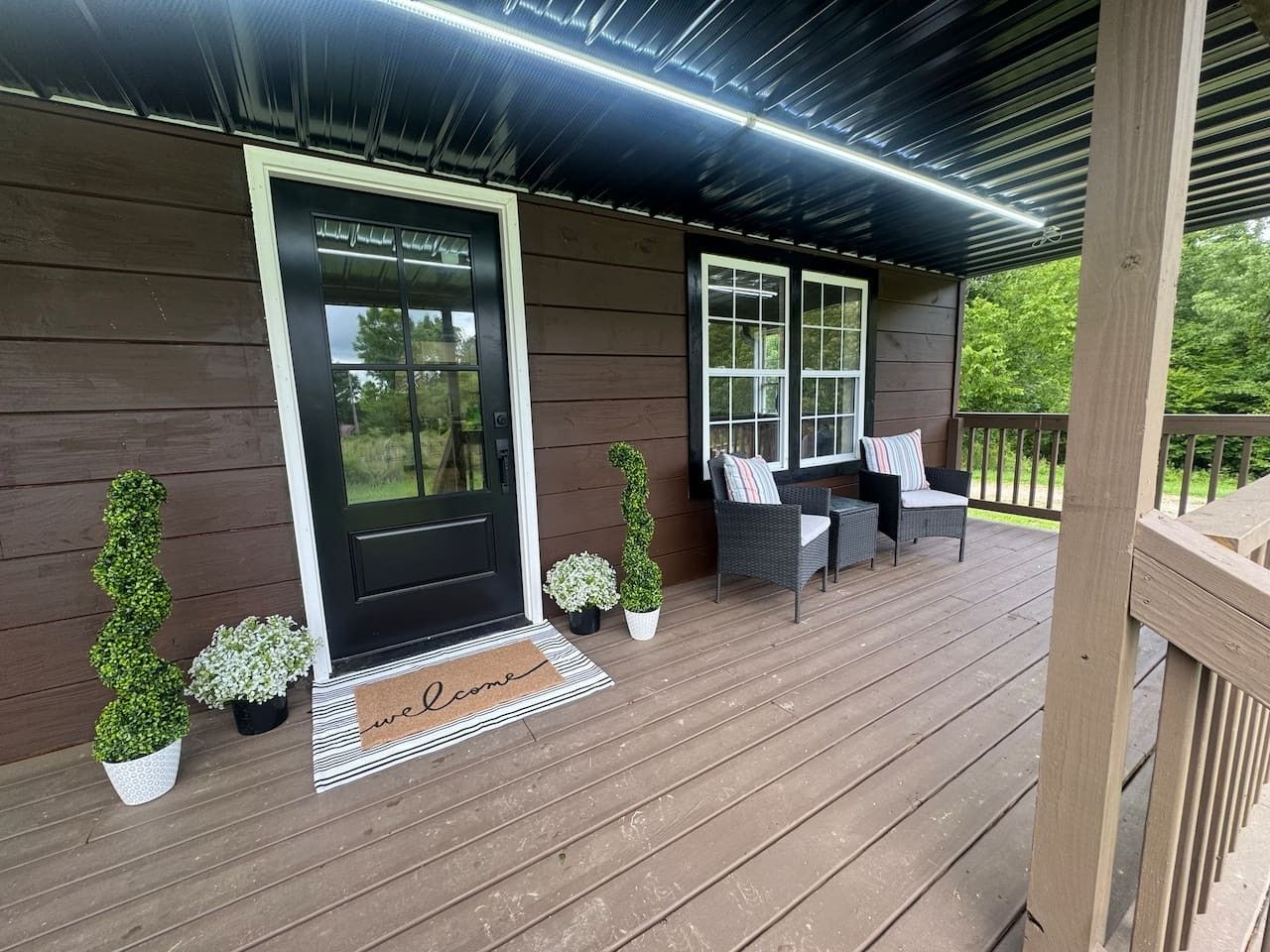 A wooden porch with a black door, two windows, and outdoor furniture.