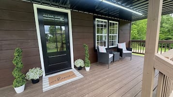 A wooden porch with a black door, two windows, and outdoor furniture.