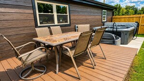 Eine Holzterrasse mit Tisch, Stühlen, einem Whirlpool und einem Grill.