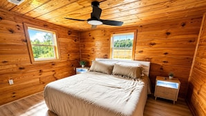 Ein Schlafzimmer mit Bett, Deckenventilator, zwei Fenstern und Holzwänden.