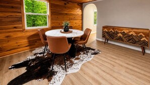 Ein Zimmer mit Holzbalkendecke, einem runden Tisch mit Stühlen, einem Kuhfellteppich und einer Bank mit Zickzackmuster.