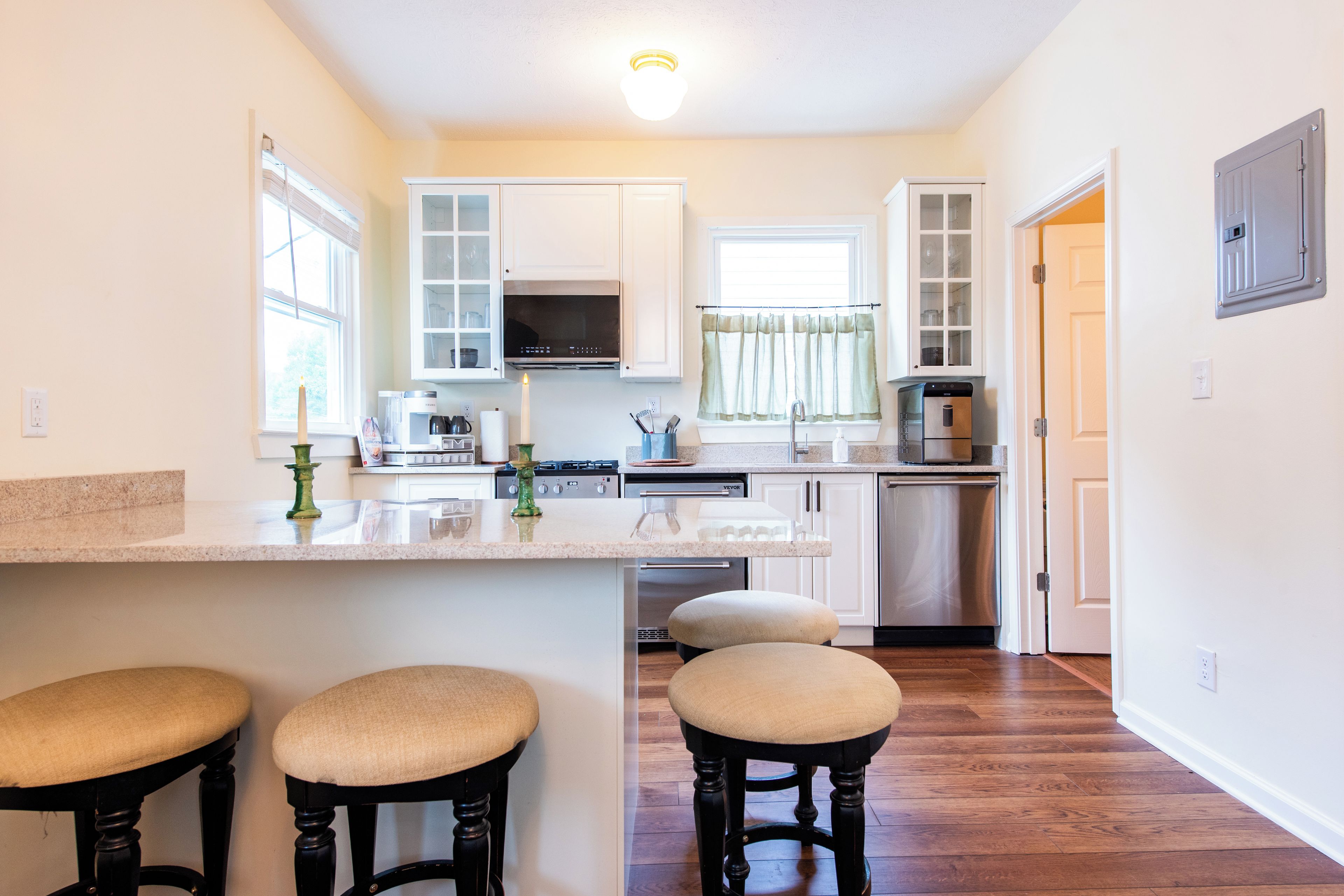A kitchen with a central island, bar stools, a microwave, a dishwasher, and a stove.