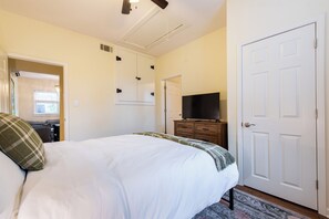 Un dormitorio con cama, cómoda, televisor y una puerta.