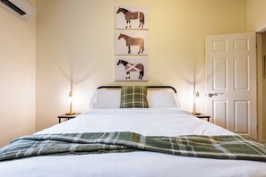 Habitación de hotel con cama, dos lámparas de noche, una puerta y tres cuadros de caballos en la pared.