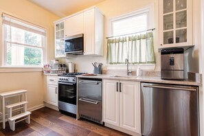 A modern kitchen with white cabinetry, stainless steel appliances, and a window with curtains. - Second-floor 2BR above Clifton's restaurant row | Stained glass, high ceilings | Rain shower, 750 Mbps | Walk everywhere (Louisville)