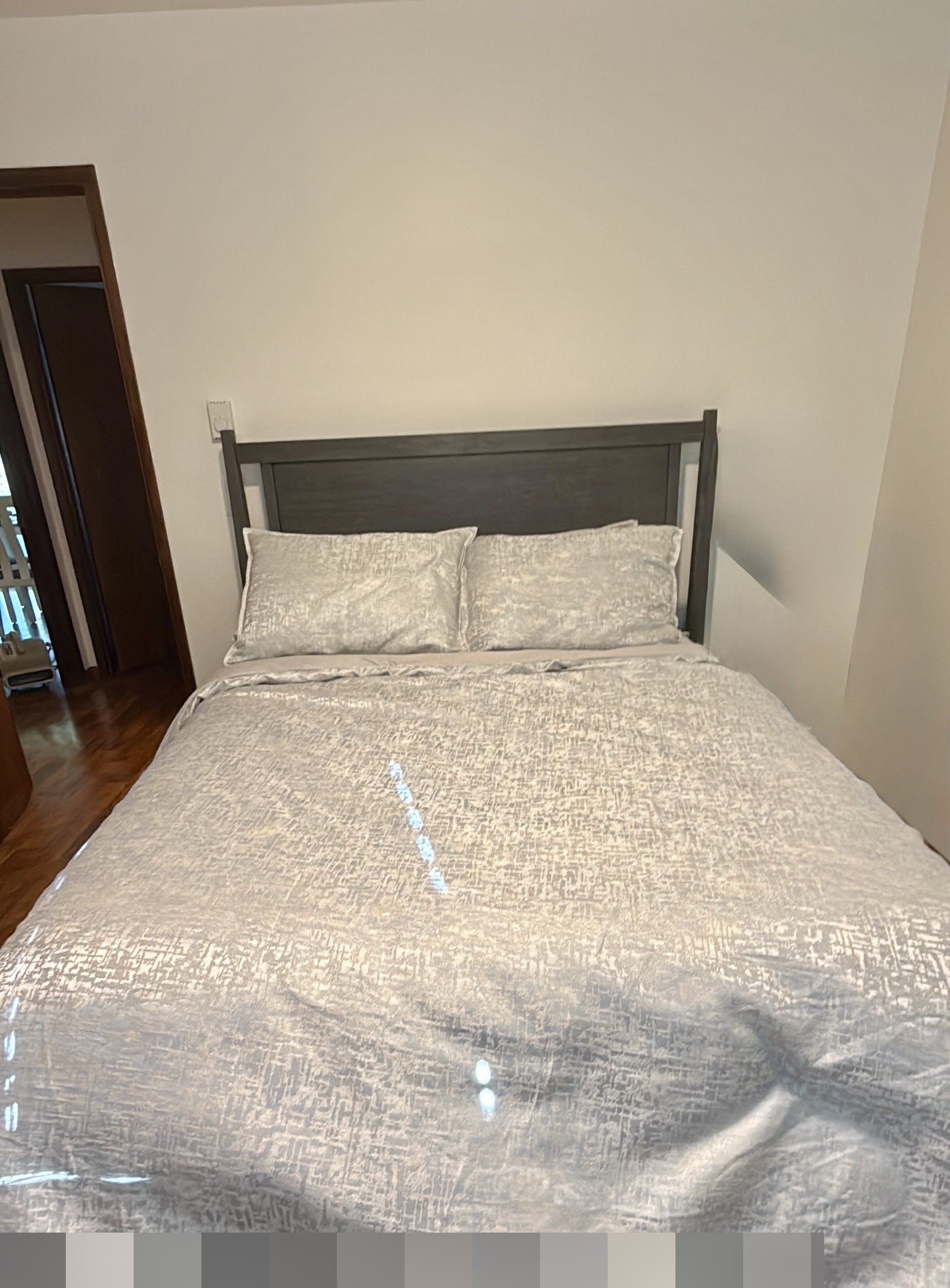 Een bed met een gestructureerd beddegoed en twee kussens, een houten hoofdbord en een effen muur.