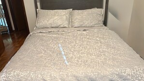 Una cama con cubrecama texturizado y dos almohadas, cabecero de madera y pared lisa.