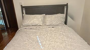 Een bed met een gestructureerd beddegoed en twee kussens, een houten hoofdbord en een effen muur.