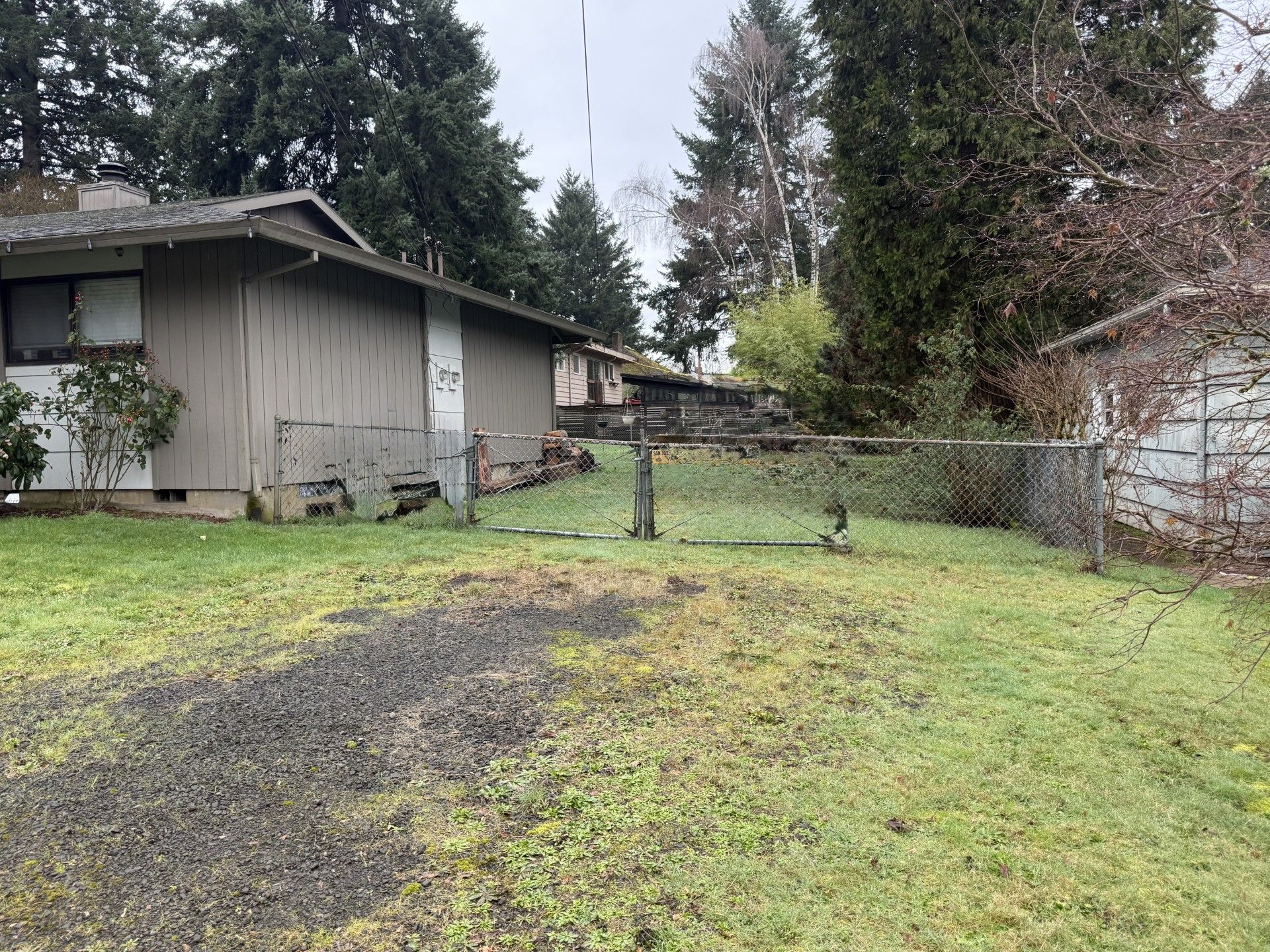 A residential property with a fenced yard, a wooden building, and a gravel driveway.