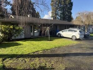 Um edifício térreo com garagem, um carro estacionado na frente e um gramado bem cuidado.