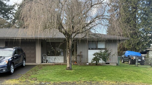 Una propiedad residencial con garaje, entrada para vehículos, césped y un árbol.