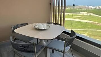 Un espace repas moderne avec une table ronde et des chaises, une vue sur la mer et un balcon équipé de stores verticaux.