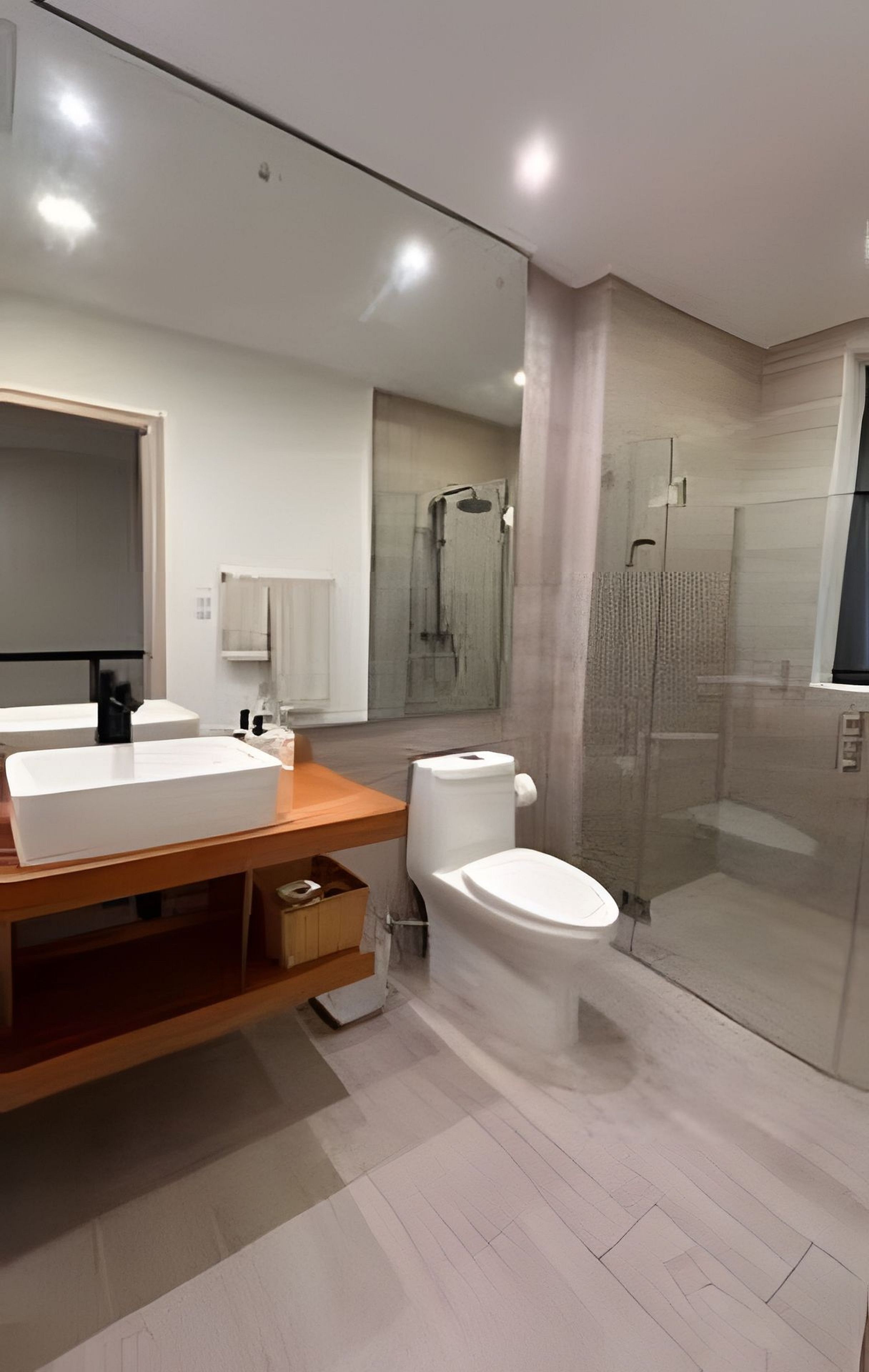 A modern bathroom with a large mirror, a wooden vanity, a toilet, and a glass-enclosed shower.
