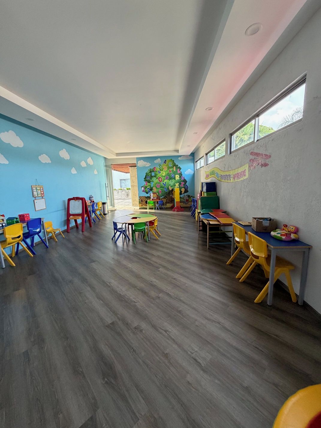 Une salle de classe avec des meubles aux couleurs vives, une fresque murale et une grande fenêtre.