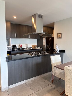 A modern kitchen with dark wood cabinets, a stainless steel range hood, and a central island with a gas stove. - Panoramic view of the volcanoes, 1 hour from Taxco and 2.5 hours from the beach (Cuernavaca)