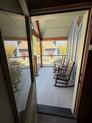 Un balcon donnant sur une maison, une porte en métal et des fauteuils à bascule en bois.