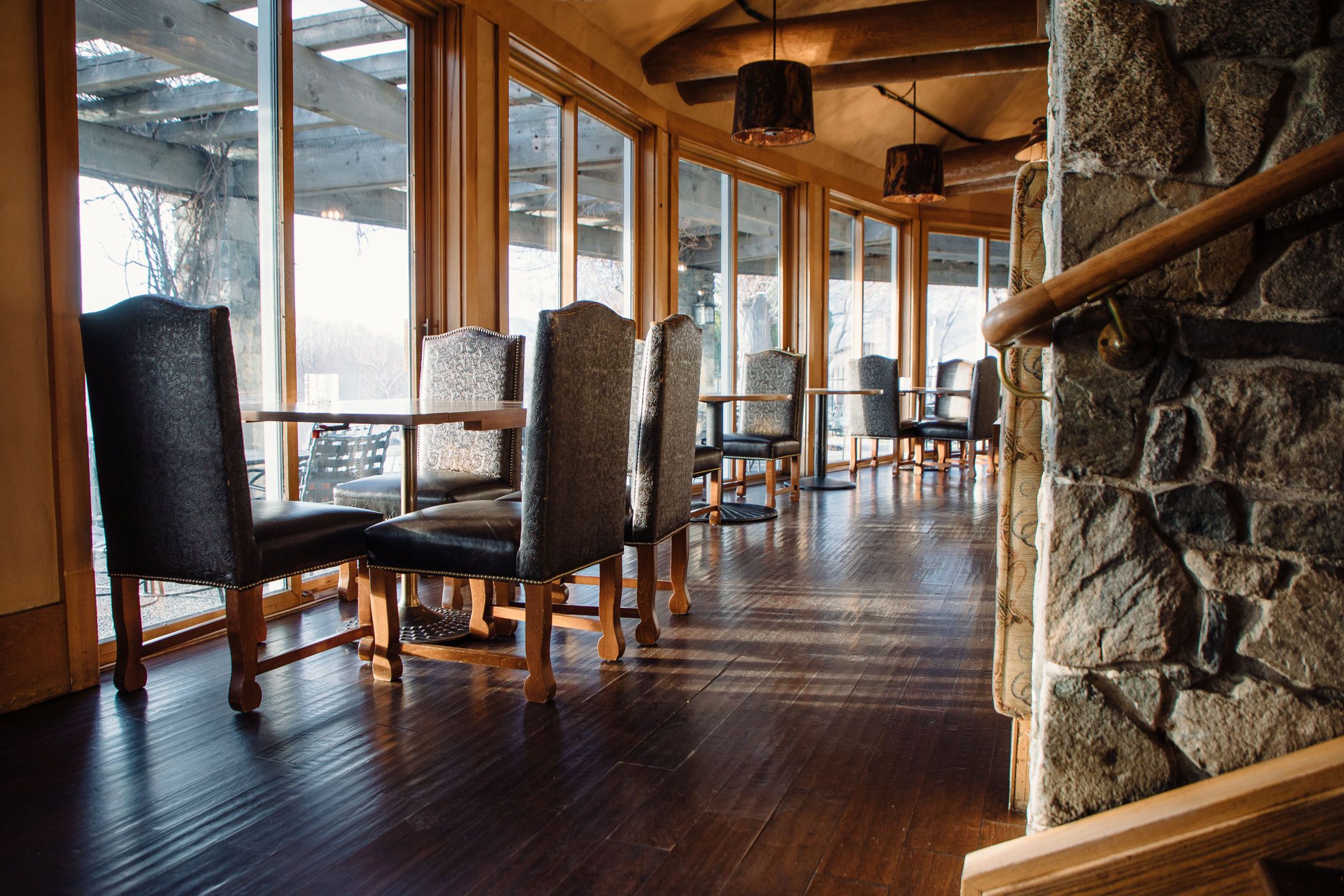 A restaurant with wooden floors, stone walls, and large windows.