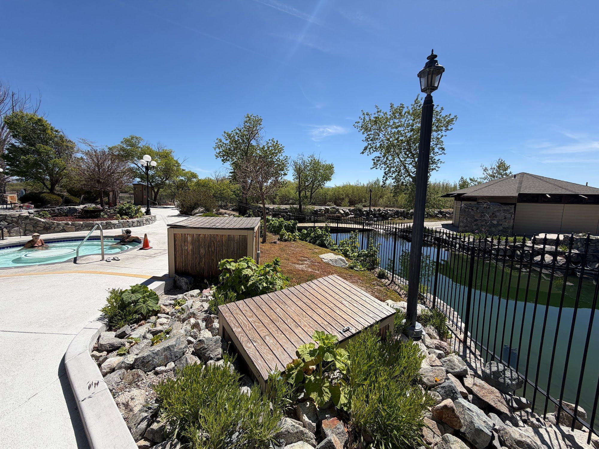 Un espace piscine avec une terrasse en bois, un petit abri de jardin et un lampadaire.