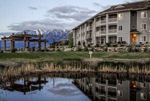 Un hôtel dont l’image se reflète dans un étang, avec un belvédère et des montagnes en arrière-plan.