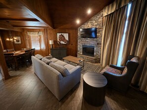 Un salon chaleureux avec une cheminée en pierre, un grand téléviseur à écran plat et un coin repas doté de meubles en bois.
