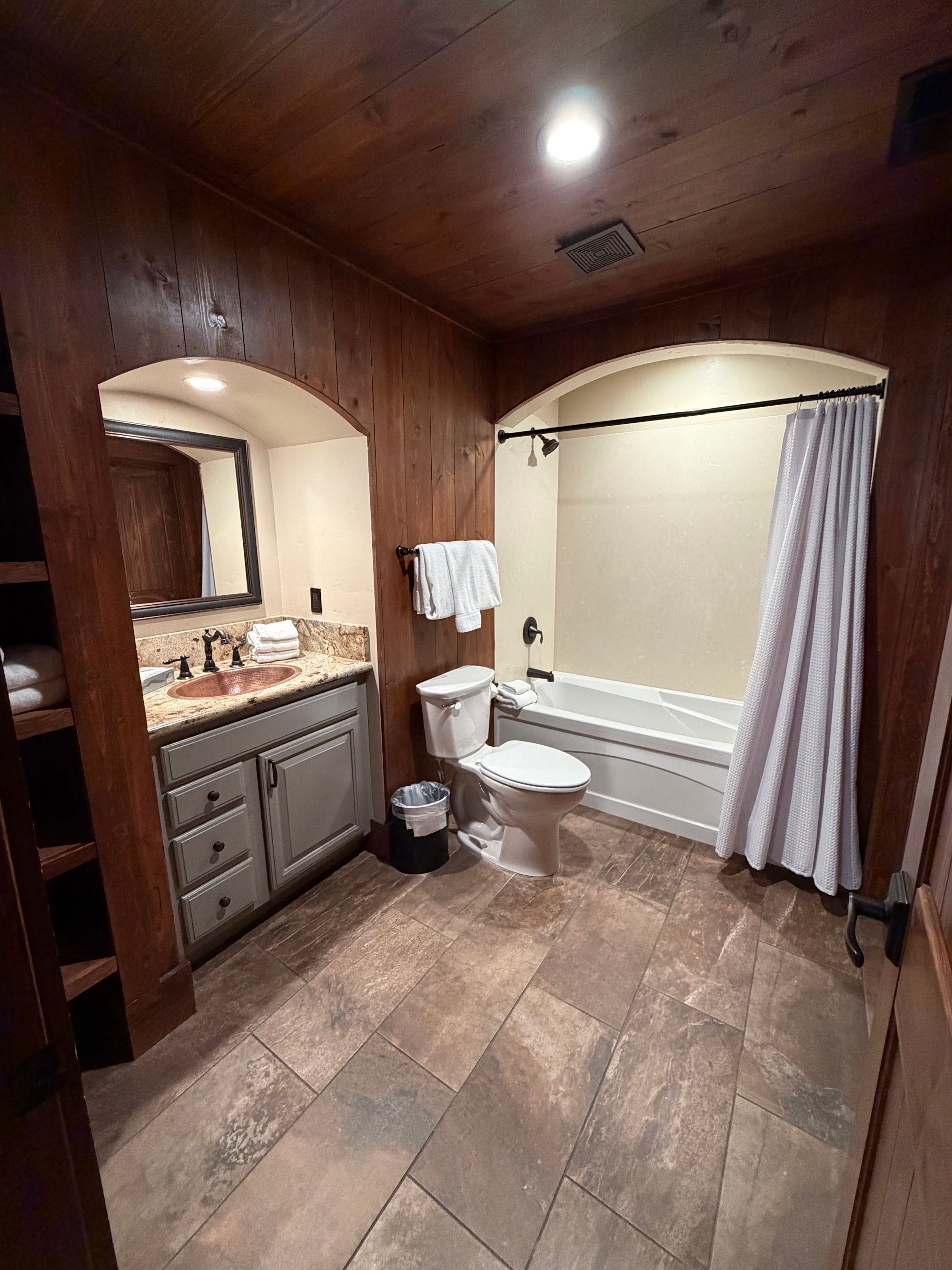 Une salle de bain avec un meuble-lavabo en bois, des toilettes, une baignoire et un rideau de douche.