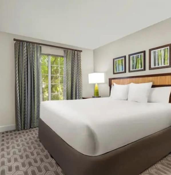 A hotel room with a large bed, a window with curtains, a bedside table with a lamp, and framed pictures on the wall. - 2-bedroom/bath Villa in fantastic Las Vegas amongst the F1 thrill (Las Vegas)