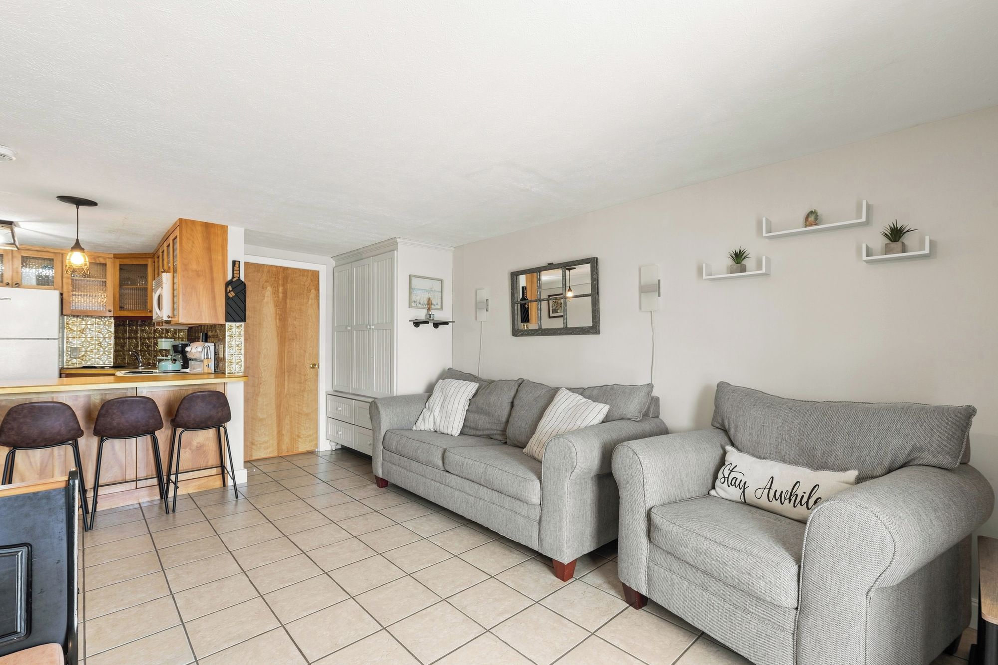 A modern living space with a kitchen, a grey sofa set, and a dining area with bar stools.