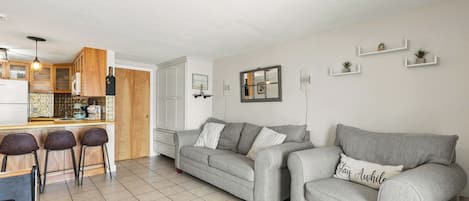 A modern living space with a kitchen, a grey sofa set, and a dining area with bar stools.