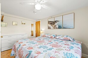 Een slaapkamer met een bed, een plafondventilator, een houten deur, een wandlamp en een lijst met een foto.