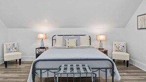 A modern bedroom with a metal bed frame, a large bed with a quilted duvet, two bedside tables with lamps, and floral-patterned chairs. - Private 1BR Retreat Among the Pines - Sleeps 4 - Unit 1 (Indian Trail)