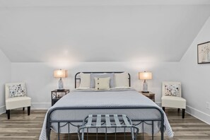 Een moderne slaapkamer met een metalen bedframe, een groot bed met een gewatteerd dekbed, twee nachtkastjes met lampen en fauteuils met bloemenprint.